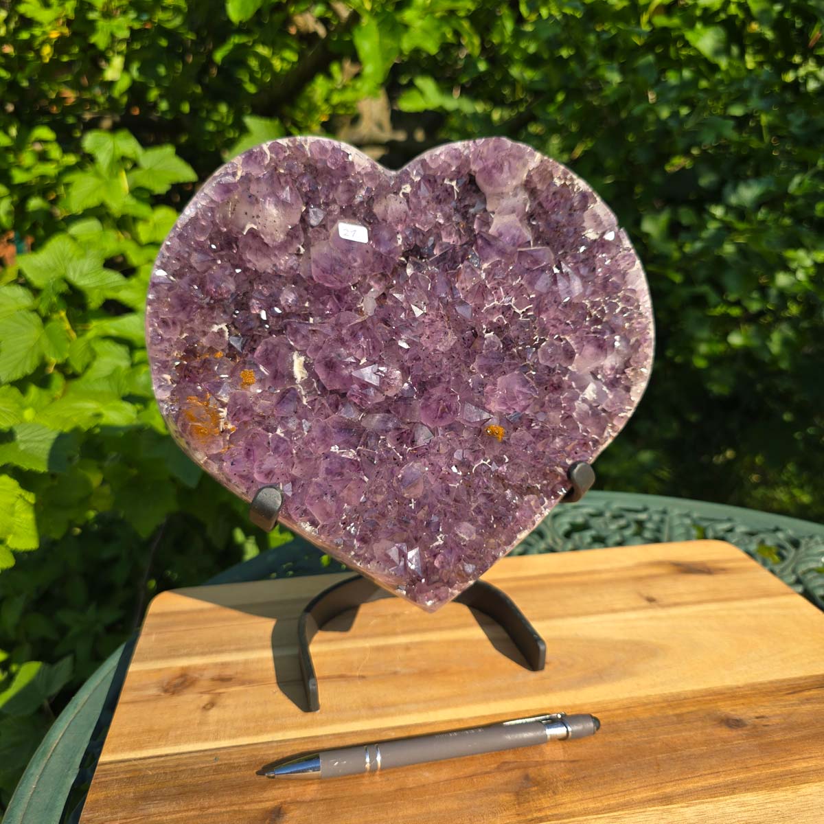 Amethyst Druse Amethyst Geode in Herzform mit Metallsockel 26x24x14cm - NR-21 auf einem Tisch im Freien.