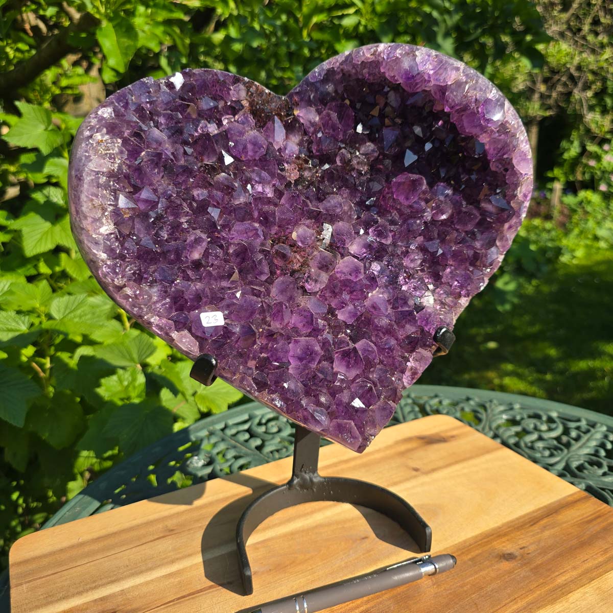 Amethyst Druse Amethyst Geode in Herzform mit Metallsockel 32x28x14cm - NR-23 auf einem stabilen Halter im Freien.
