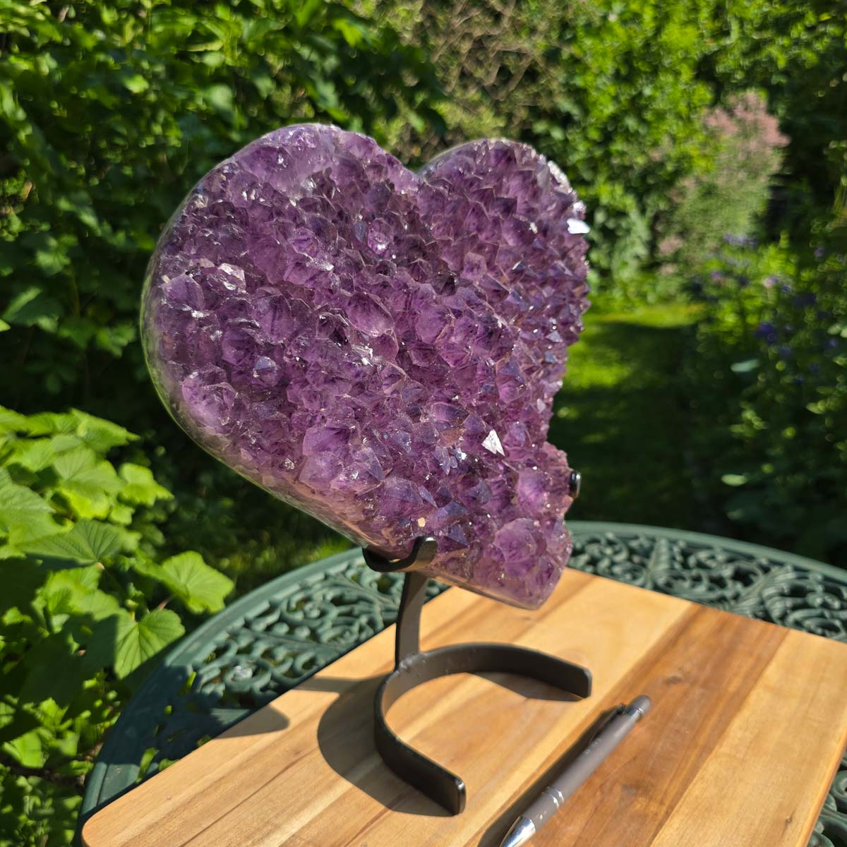 Amethyst Druse Amethyst Geode in Herzform mit Metallsockel 31x28x12cm - NR-24 auf einem Tisch im Freien.