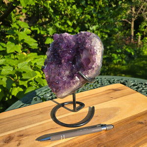 Amethyst Druse Amethyst Geode in Herzform mit Metallsockel 19x16x11cm - NR-36 auf einem Tisch im Freien.