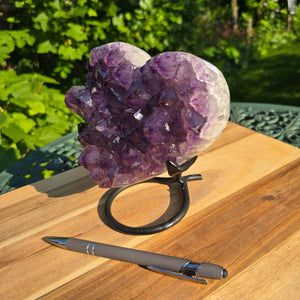 Amethyst Druse Amethyst Geode in Herzform mit Metallsockel 15x14x12cm - NR-40 auf einem Tisch im Freien.