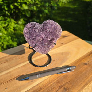 Amethyst Druse Amethyst Geode in Herzform mit Metallsockel 12x9x8cm - NR-49 auf Holztablett neben einem Stift.