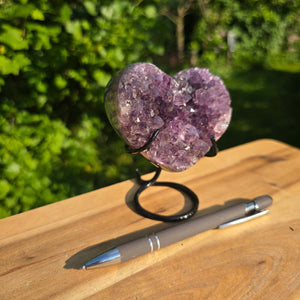 Amethyst Druse Amethyst Geode in Herzform mit Metallsockel 10x9x8cm - NR-56 auf einem Holztisch, neben einem Stift.