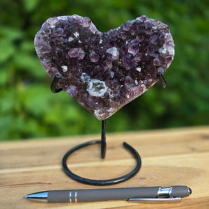 Amethyst Druse Amethyst Geode in Herzform mit Metallsockel 17x14x10cm - NR-64 auf einem Tisch mit Stift.
