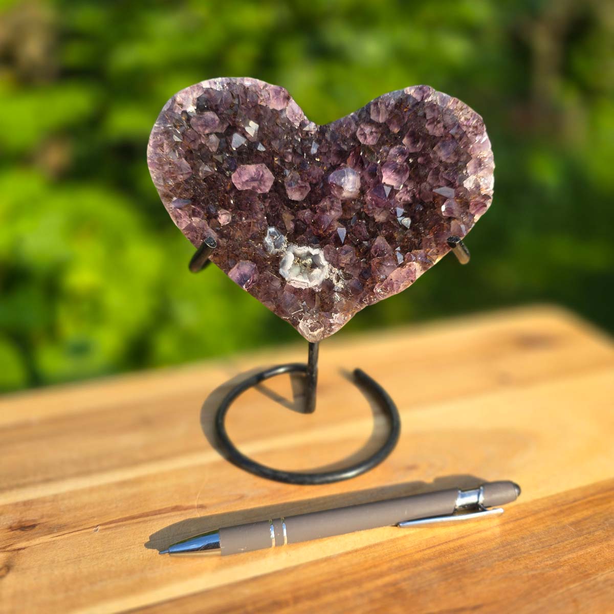 Amethyst Druse Amethyst Geode in Herzform mit Metallsockel 17x14x10cm - NR-64 auf einem Tisch mit Stift.