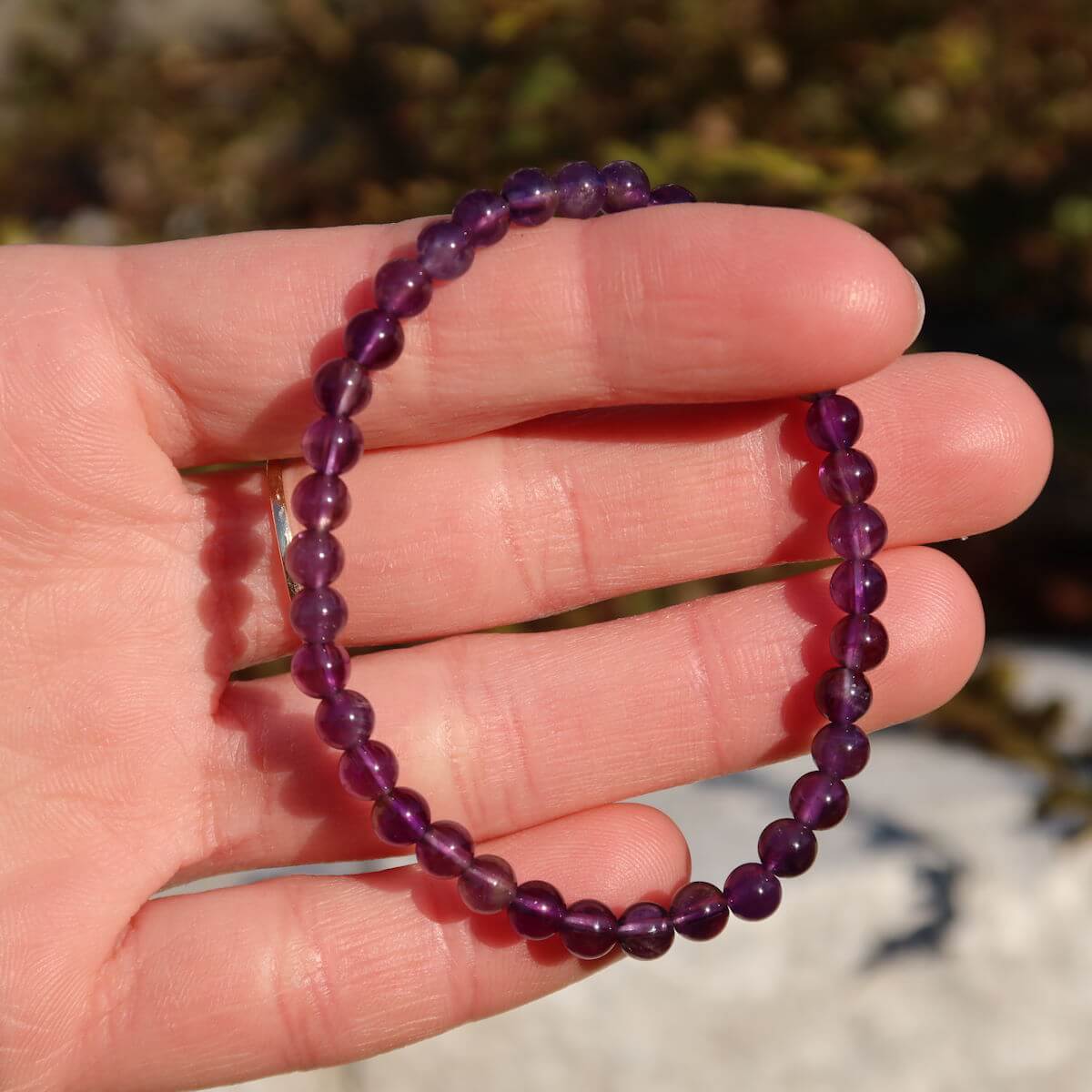 Hand holding amethyst bracelet in vibrant violet, available at Online Shop Steinwelten Graz and Wiener Neustadt, sizes 4-6-8mm.