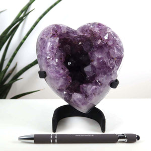 Amethyst Druse Amethyst Geode in Herzform mit Metallsockel 10x11cm - NR-13 auf weißem Tisch vor Pflanzen