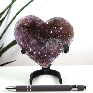 Amethyst Druse Amethyst Geode in Herzform mit Metallsockel 10x12cm - NR-7, präsentiert auf einem Schreibtisch, neben einem Stift.