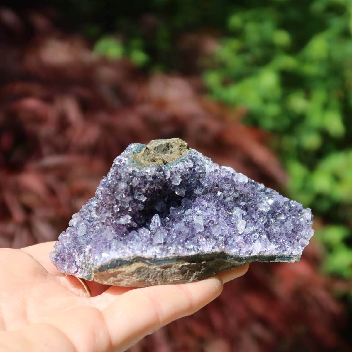 Hand holding amethyst druse with unique crystal formations against a natural background, representing harmony and spirituality.