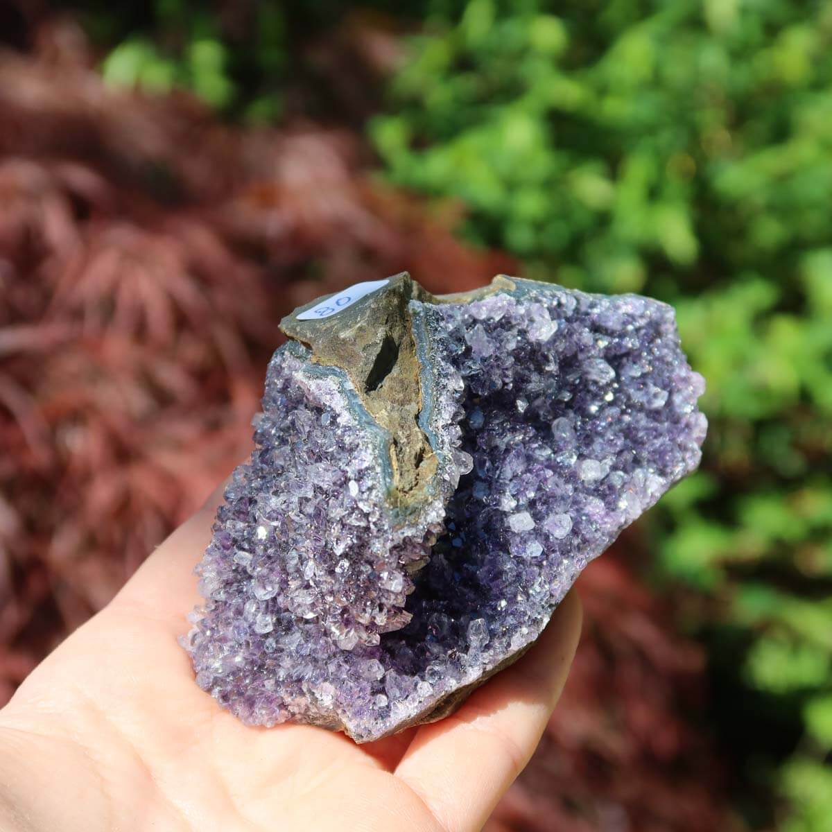 Hand holding amethyst druse with unique crystal formations against a natural background, representing harmony and spirituality.
