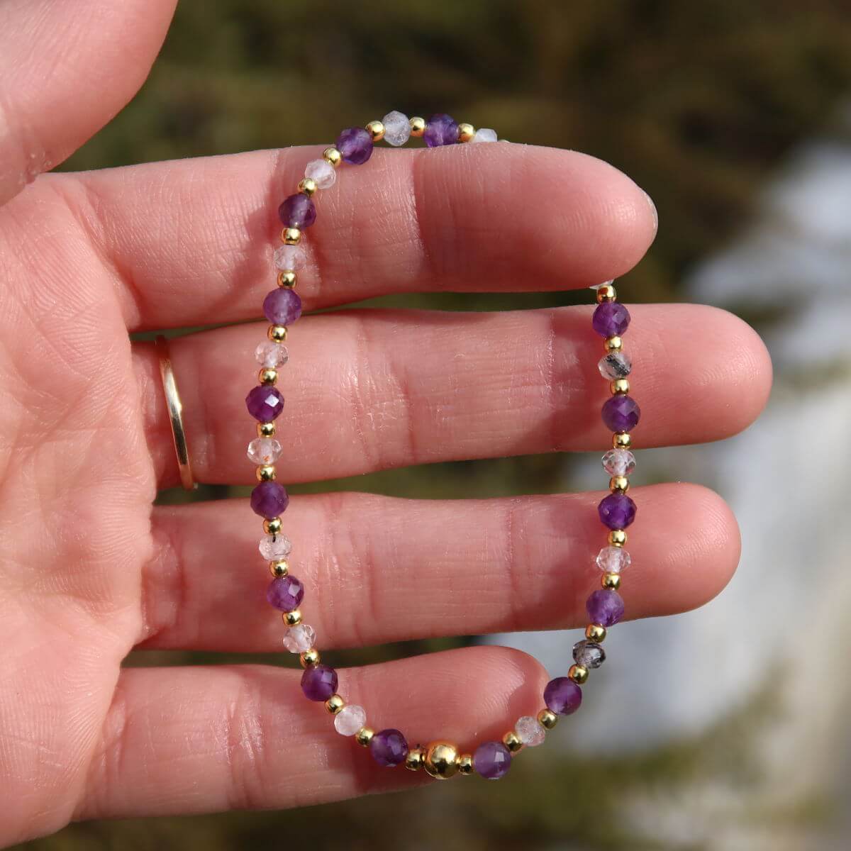 Handmade amethyst and tourmaline quartz faceted gemstone bracelet on wrist, showcasing its vibrant purple and clear stones.