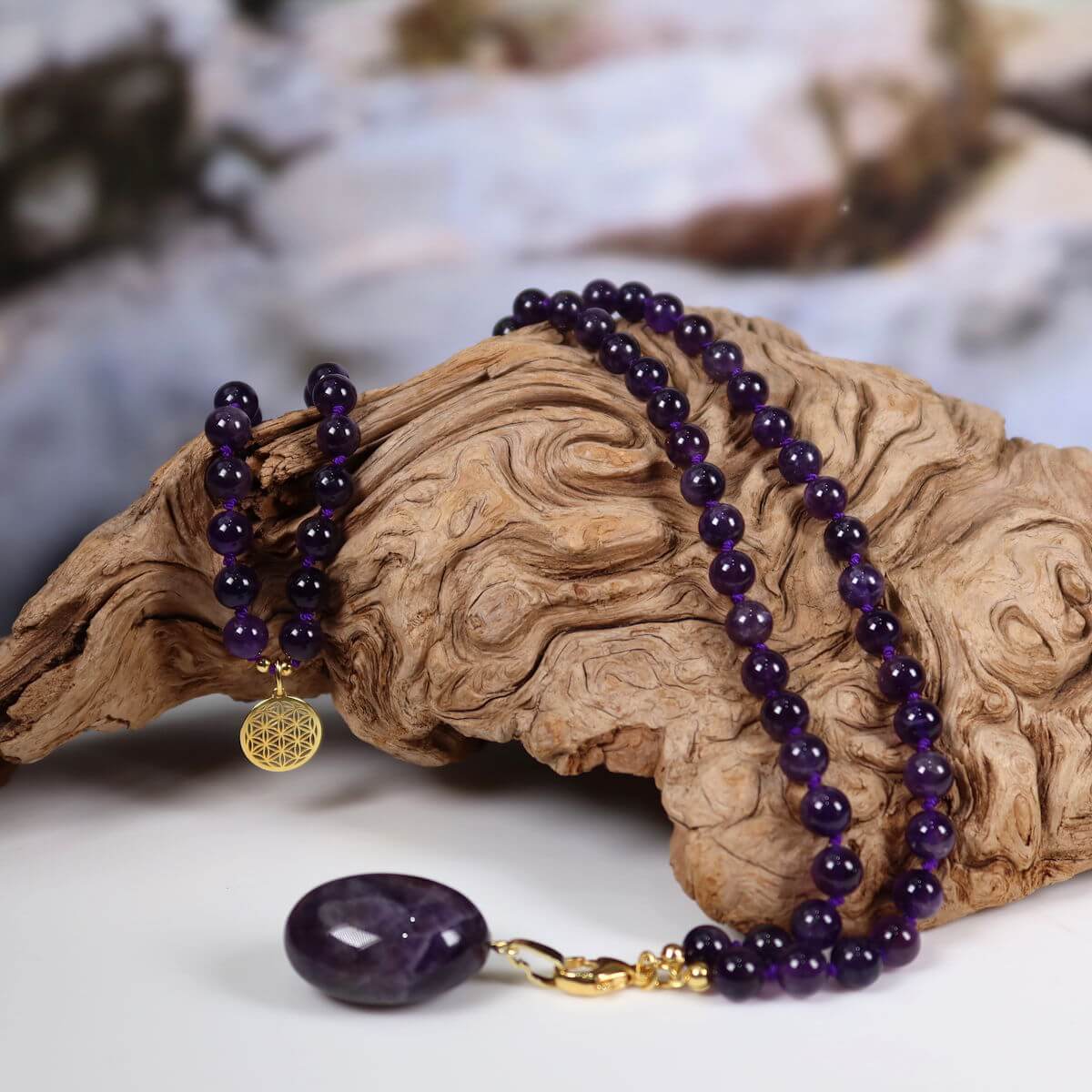 Hand-knotted amethyst necklace with unique pendant "Blume des Lebens" on wood; Steinwelten jewelry for harmony and transformation.