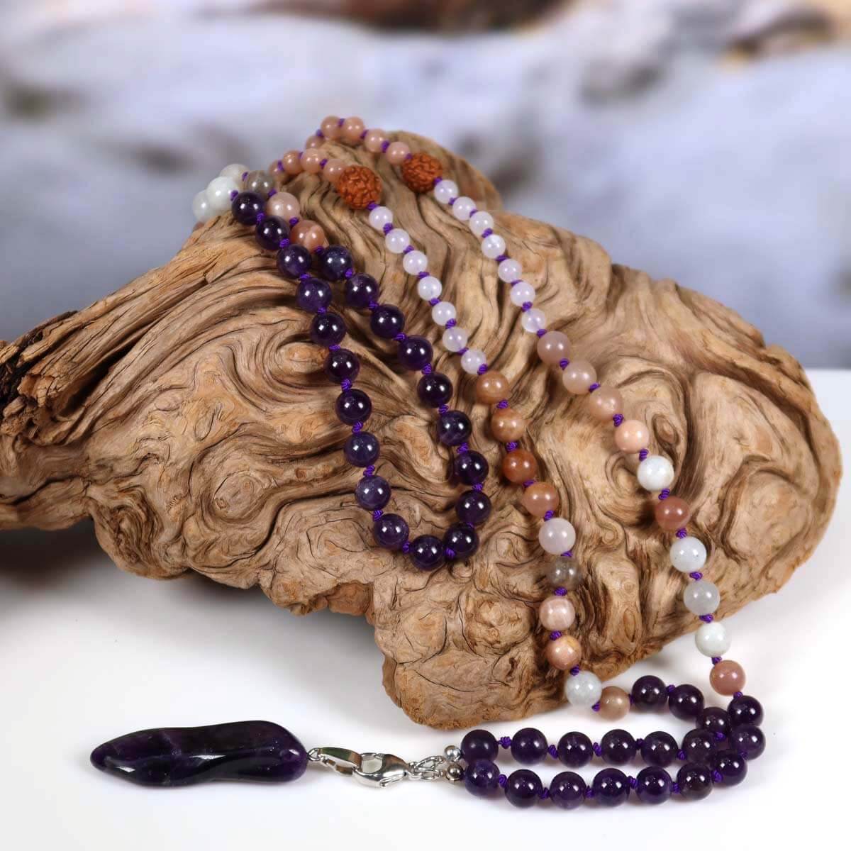 Handcrafted mala necklace with amethyst, moonstone, labradorite, rudraksha beads and amethyst pendant on driftwood display.