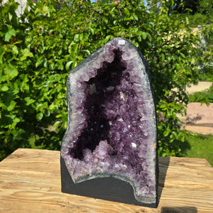 Amethyst Druse – Geode - 38x35x21cm und 21,2kg – Steinwelten OG - Nr. 167 on rustic wooden table, lush garden background