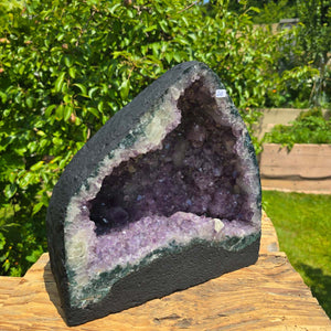 Amethyst Druse – Geode - 28x28x16cm und 12,4kg – Steinwelten OG - Nr. 258 displayed on a wooden surface outdoors.