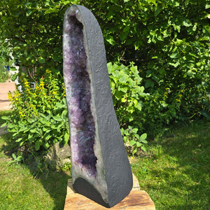 Amethyst Druse – Geode - 84x25x25cm und 46,2kg – Steinwelten OG - Nr. 359 displayed outdoors against greenery.