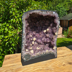 Amethyst Druse – Geode - 43x32x22cm und 31,2kg – Steinwelten OG - Nr. 53 on wooden table in a green garden setting.