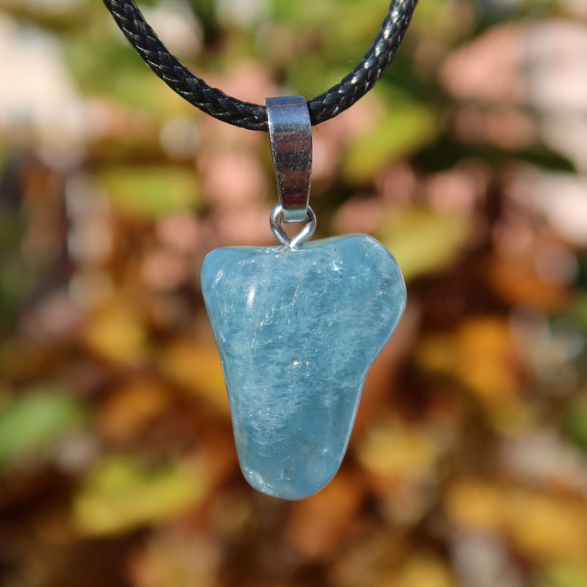 1A Qualität Aquamarin Anhänger 25mm - Ausgeglichenheit und frische Energie - UNIKAT Nr. 15, hellblauer Stein mit Lederband vor Herbstlaub