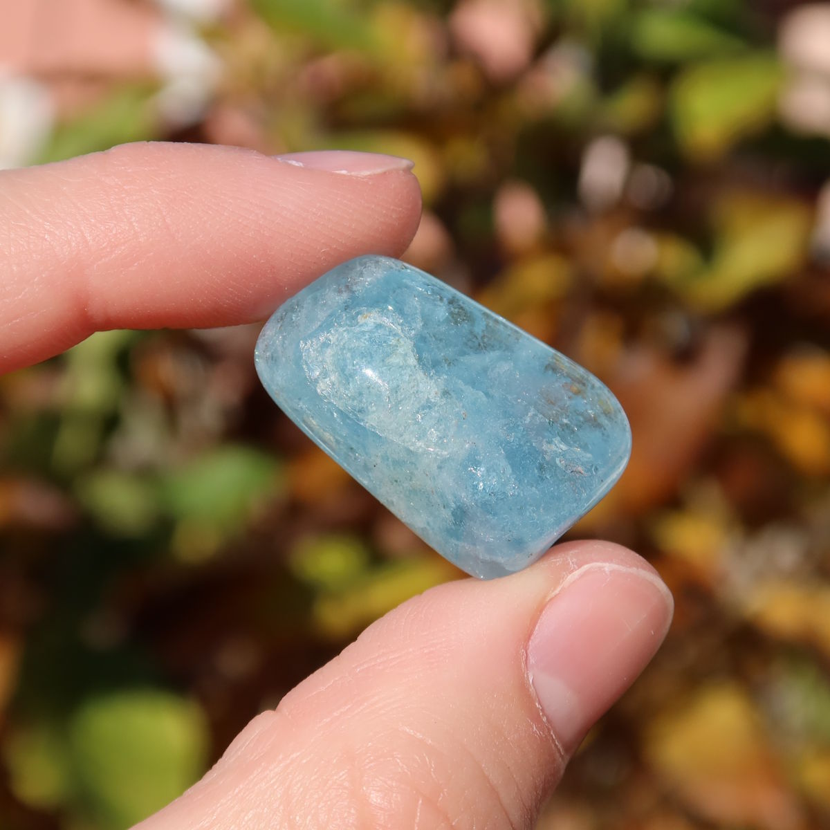 Hand holding 1A Qualität Aquamarin Handschmeichler 25mm - Ausgeglichenheit und frische Energie - UNIKAT Nr. 14 in sunlight