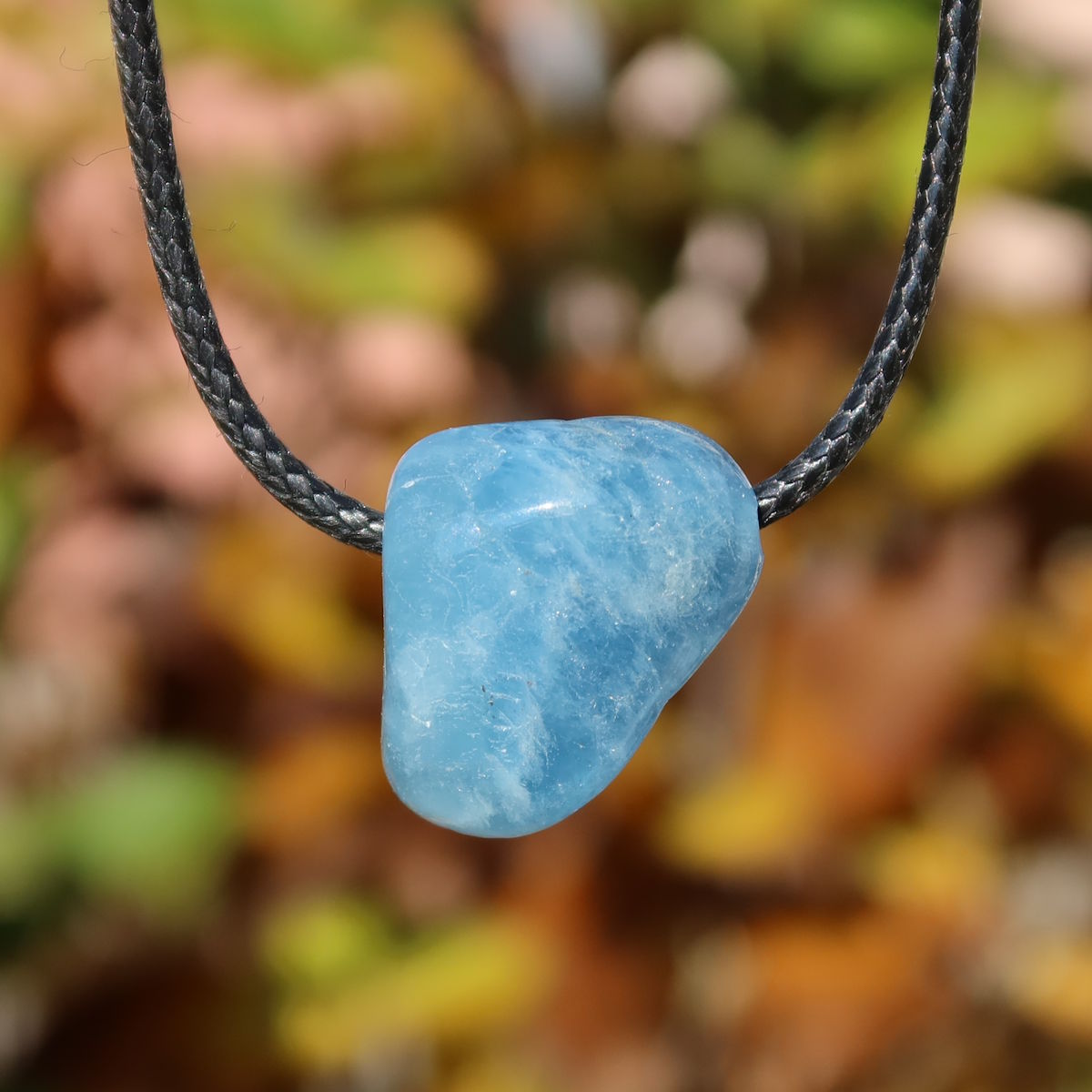 1A Qualität Aquamarin gebohrt 26mm - Ausgeglichenheit und frische Energie - UNIKAT Nr. 10, hellblauer Anhänger vor buntem Hintergrund