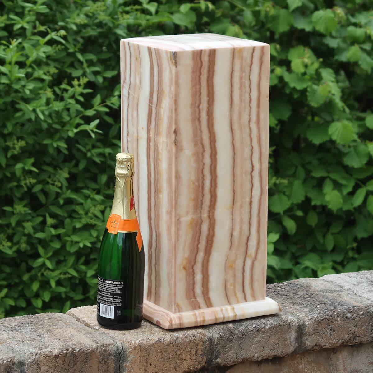 Large Aragonit lamp with LED, handcrafted in Morocco, beside a champagne bottle for scale against a lush green background.