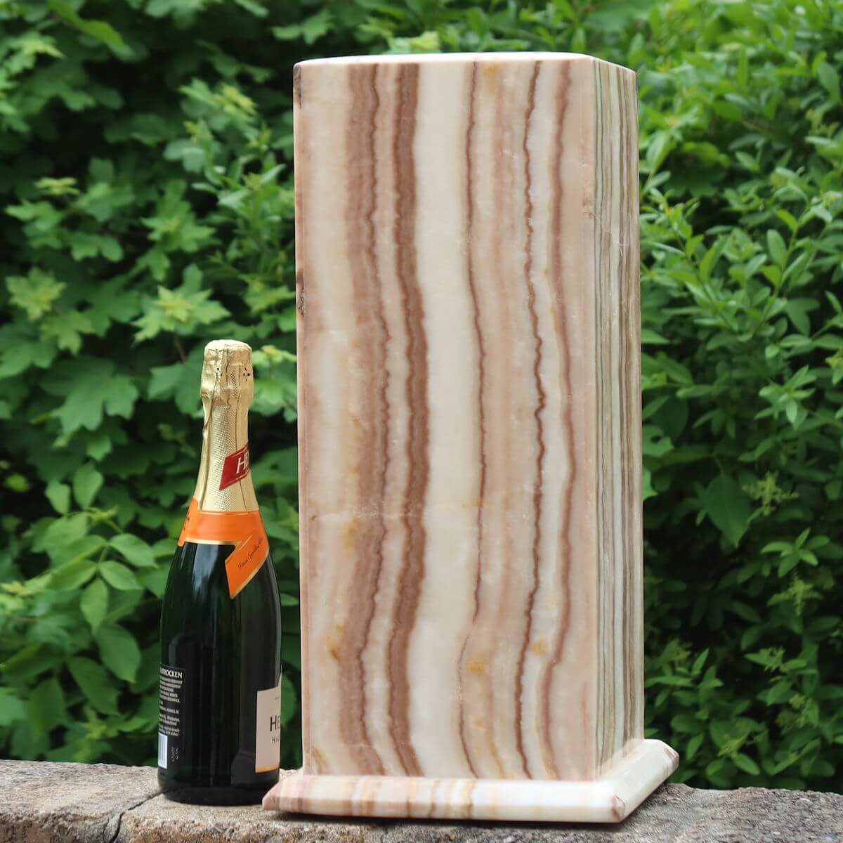 Large Aragonit lamp with LED, handcrafted in Morocco, beside a champagne bottle for scale against a lush green background.