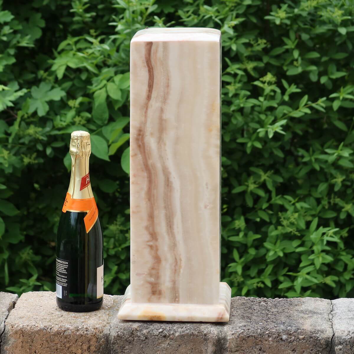Aragonite stone lamp from Morocco with LED and champagne bottle for size comparison, outdoors with greenery background.