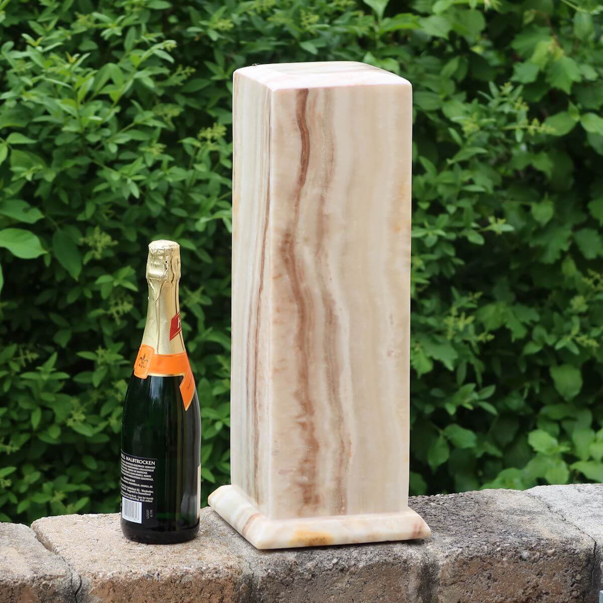 Aragonite stone lamp from Morocco with LED and champagne bottle for size comparison, outdoors with greenery background.