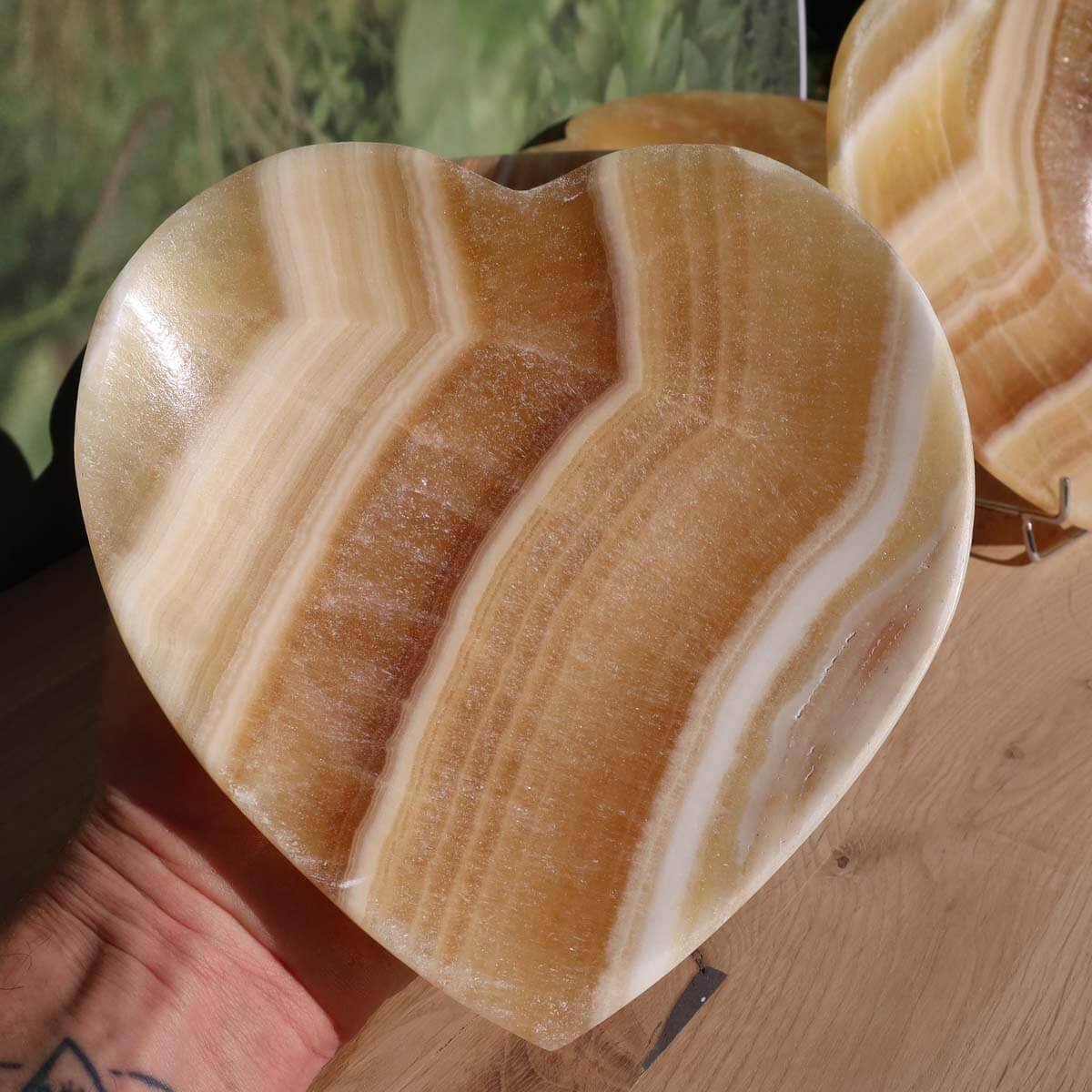 Herzförmige Aragonit-Onyx Schale, 16 cm groß, dekorativer Edelstein aus Marokko auf Holzdisplay. Produkt von Steinwelten Graz.