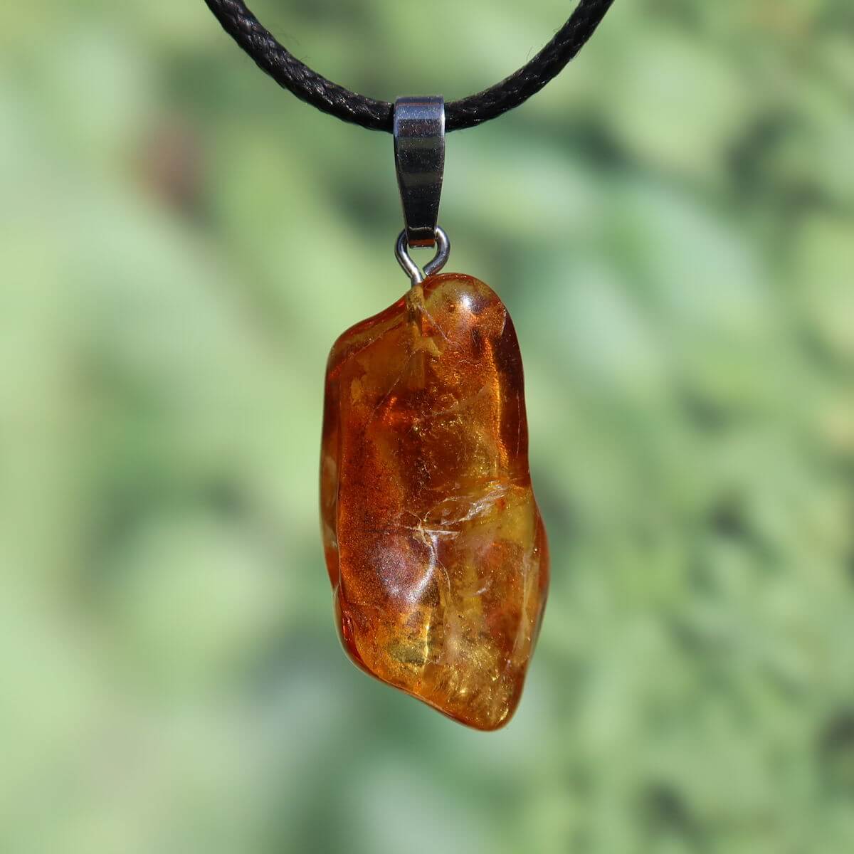 Natürlicher Bernstein Anhänger 35mm, UNIKAT Nr. 11, leuchtend im Licht auf schwarzer Halskette, symbolisiert Lebensfreude und Selbstwert.