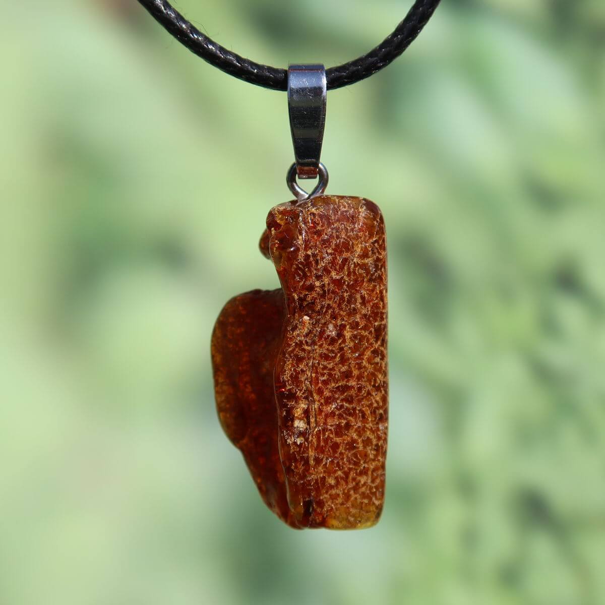 Natürlicher Bernstein Anhänger 32mm Unikat Nr. 15, symbolisiert Lebensfreude und Selbstwert, vor grünem Hintergrund.