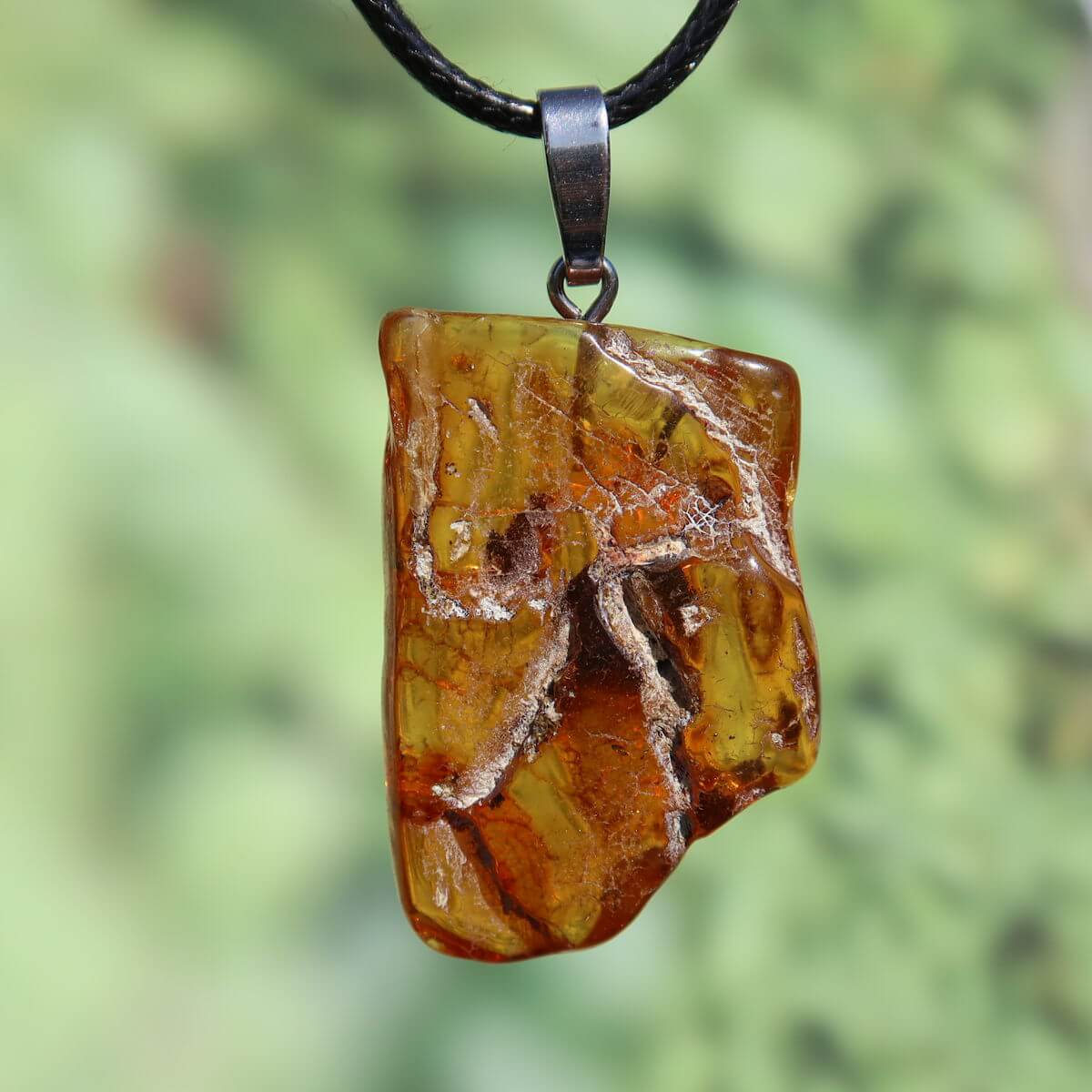 Natürlicher Bernstein Anhänger 38mm mit einzigartiger Pflanzenharzstruktur, UNIKAT Nr. 25, schimmernd bei Lichteinfall, auf schwarzem Halsband.