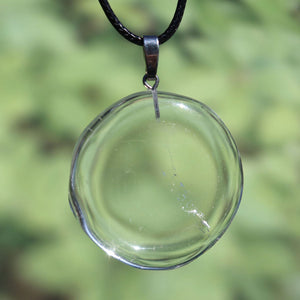 Bergkristall Anhänger 42mm mit klarer Struktur, ideal für Fokussierung und Stabilität, aufgehängt an einer schwarzen Kordel vor grünem Hintergrund.