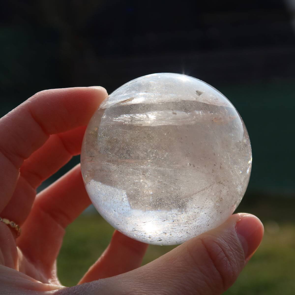 Bergkristall Kugel geschliffen UNIKAT Nr. 1, erhältlich im Online Shop Steinwelten Graz und Wiener Neustadt, handgehalten vor grünem Hintergrund.