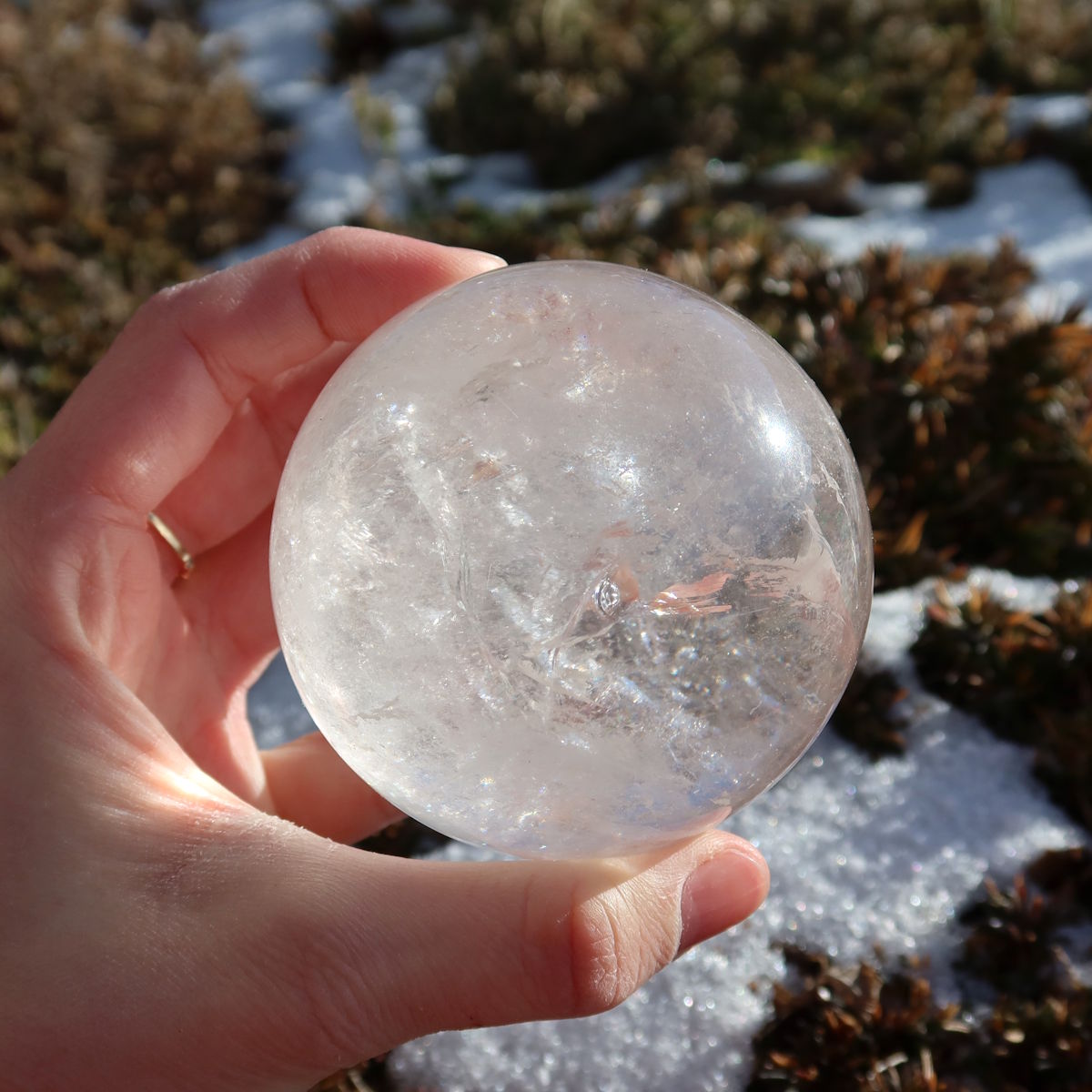 Bergkristall Kugel – Natürliche Kristallkugel 70mm Durchmesser Nr. 34 in der Hand gehalten mit natürlichem Licht im Freien.