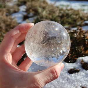 Das Bild zeigt eine Bergkristall Kugel – Natürliche Kristallkugel 65mm Durchmesser Nr. 35, die im Sonnenlicht gehalten wird.