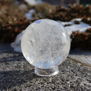 Bergkristall Kugel – Natürliche Kristallkugel 65mm Durchmesser Nr. 37 auf einem Stein, von der Sonne beleuchtet