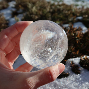 Hand holding Bergkristall Kugel – Natürliche Kristallkugel 60mm Durchmesser Nr. 38 made of natural crystal outdoors