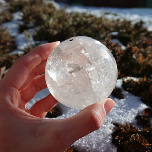 Bergkristall Kugel – Natürliche Kristallkugel 60mm Durchmesser Nr. 39 in der Hand vor einem winterlichen Hintergrund