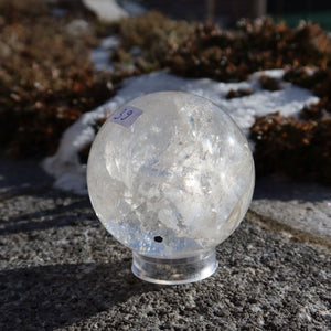 Bergkristall Kugel – Natürliche Kristallkugel 60mm Durchmesser Nr. 39 auf Steinuntergrund in hellem Sonnenlicht.