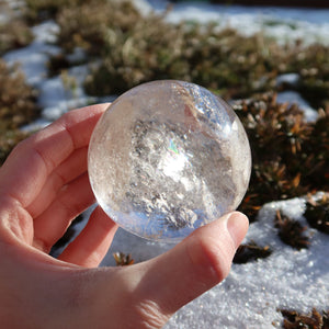 Bergkristall Kugel – Natürliche Kristallkugel 60mm Durchmesser Nr. 41 in Hand, zeigt klare Textur und Farbspiel in der Sonne.