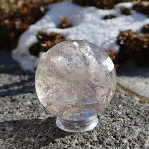 Bergkristall Kugel – Natürliche Kristallkugel 60mm Durchmesser Nr. 41, klare Kristallkugel auf Steinoberfläche mit winterlicher Kulisse