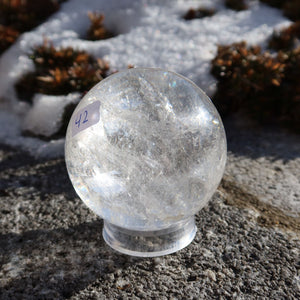 Bergkristall Kugel – Natürliche Kristallkugel 55mm Durchmesser Nr. 42 auf einem Steinuntergrund, lichtdurchlässig und funkelnd.