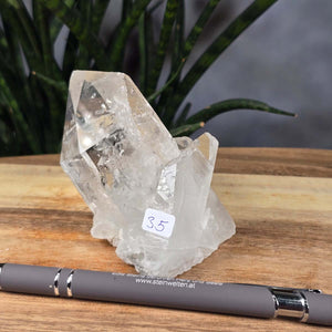 Bergkristall Stufe 1A Qualität, 7x8x5 cm - Klarheit und Fokus - UNIKAT Nr. 35: Brazilian clear quartz crystal on wooden surface with pen.