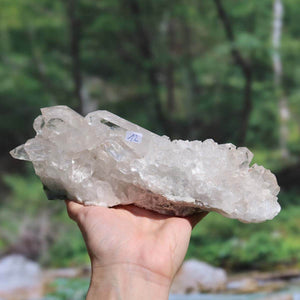 Hand holding a natural, raw Brazilian quartz crystal cluster with clear and milky inclusions, showcasing unique growth structures.