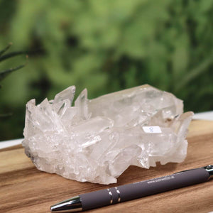 Bergkristall Stufe 1A, 0.8kg, naturbelassen, auf Holzbrett neben Stift, ideale Dekoration für Klarheit und Fokus.