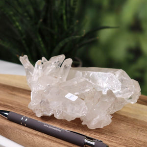 Natural Brazilian Bergkristall crystal cluster on wooden surface, showcasing clear and milky inclusions, with pen for size reference.