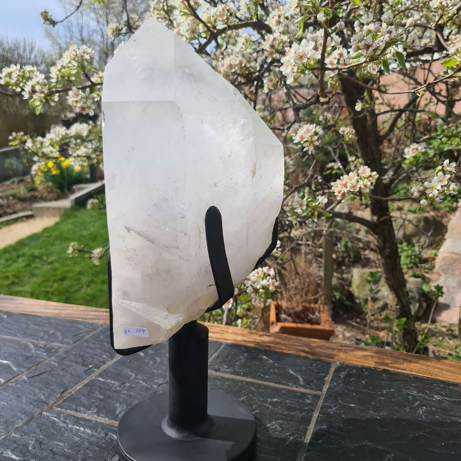 Natürlicher Bergkristall XL auf Metallständer im Freien vor blühendem Baum, ideal für Raumdekoration und Meditation.