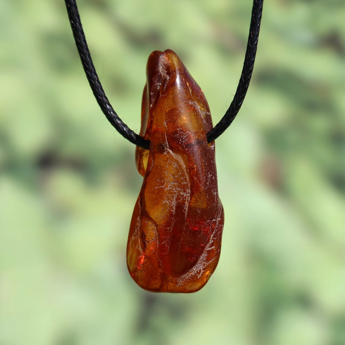 Natural amber pendant, 48mm, unique UNIKAT No. 10, showcasing transparency and shine in sunlight on a black cord.