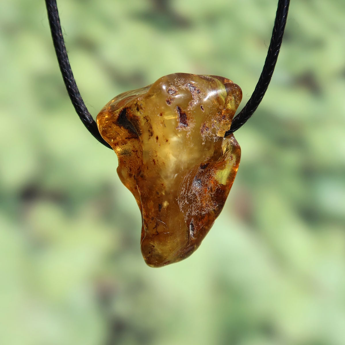 Unique natural amber pendant with drilled hole, 35mm, symbolizing joy and confidence, displayed on a black cord.